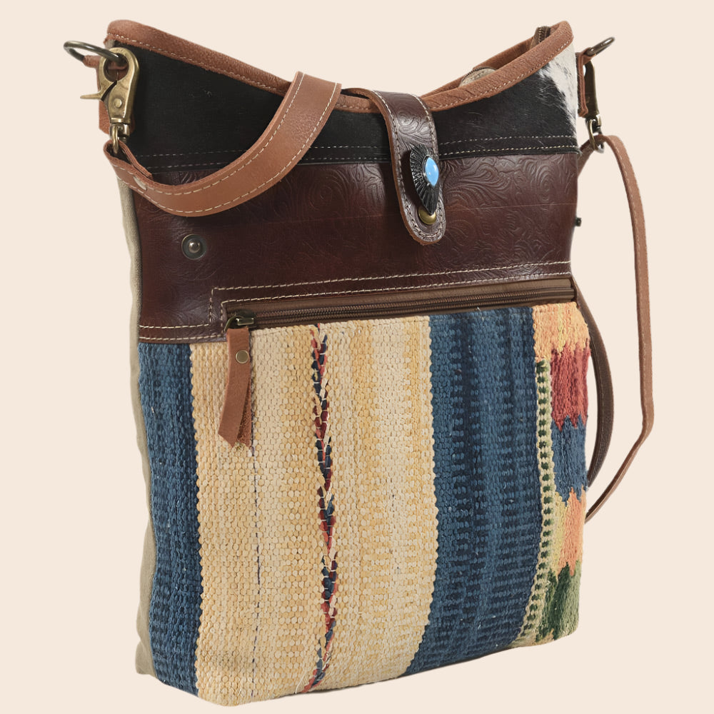 Multicolored patterned handbag with brown leather accents on a white background