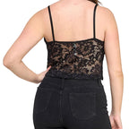 A woman shown from the back wearing a black lace spaghetti-strap camisole top and black jeans against a light gray studio background.