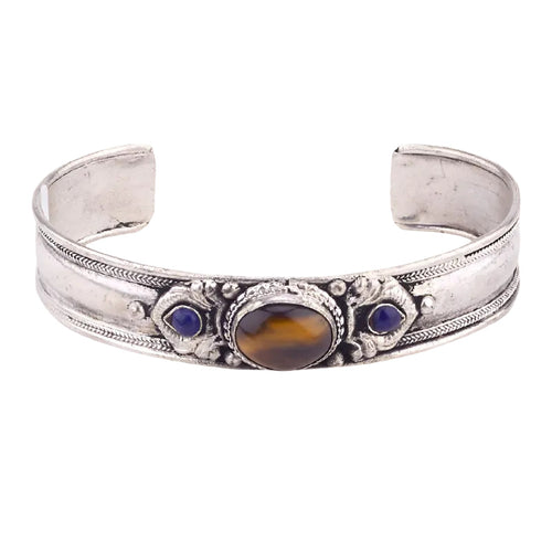 An antique-style silver cuff bracelet featuring a central oval brown tiger's eye stone and two small round blue gemstone accents, set against a plain white background.
