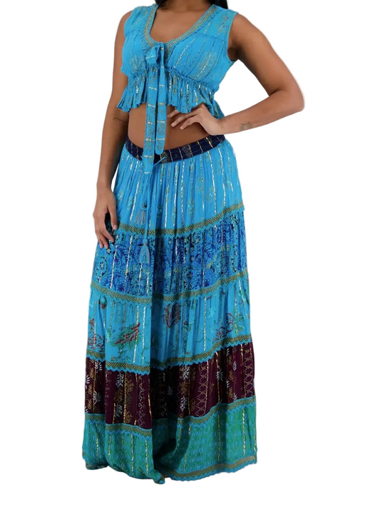 A woman modeling a two-piece bohemian-style outfit featuring a turquoise blue tie-front crop top and a matching tiered maxi skirt with a dark waistband and multicolored patterned borders.