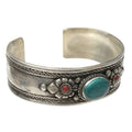 A silver cuff bracelet with turquoise and red accents, featuring leaf patterns and floral designs.