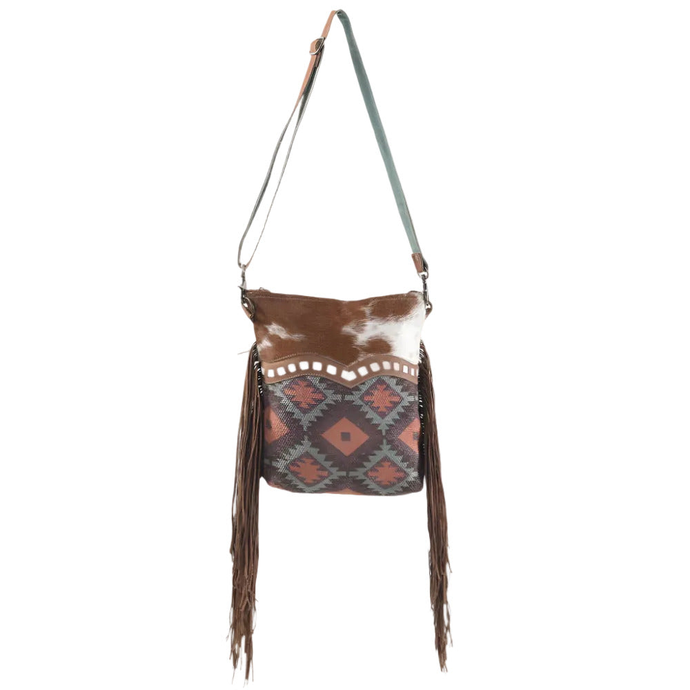 Brown and white cowhide bag with patterned flap and fringes on a white background