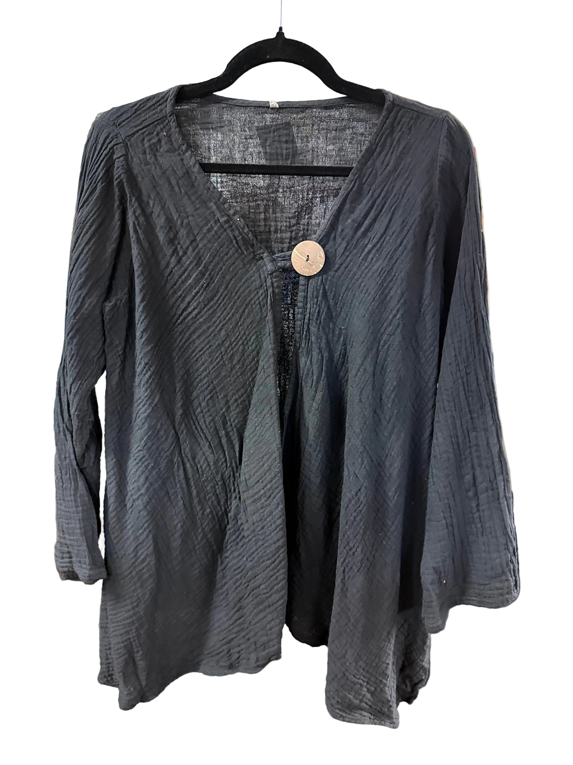 A black textured long-sleeve top with a V-neck and a single wooden button closure, hanging on a black hanger on a white background.