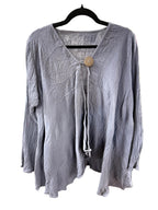 A crinkled, long-sleeve lavender-gray blouse hanging on a black hanger on a white background. It features a split V-neckline with a central tie and a single large wooden button.