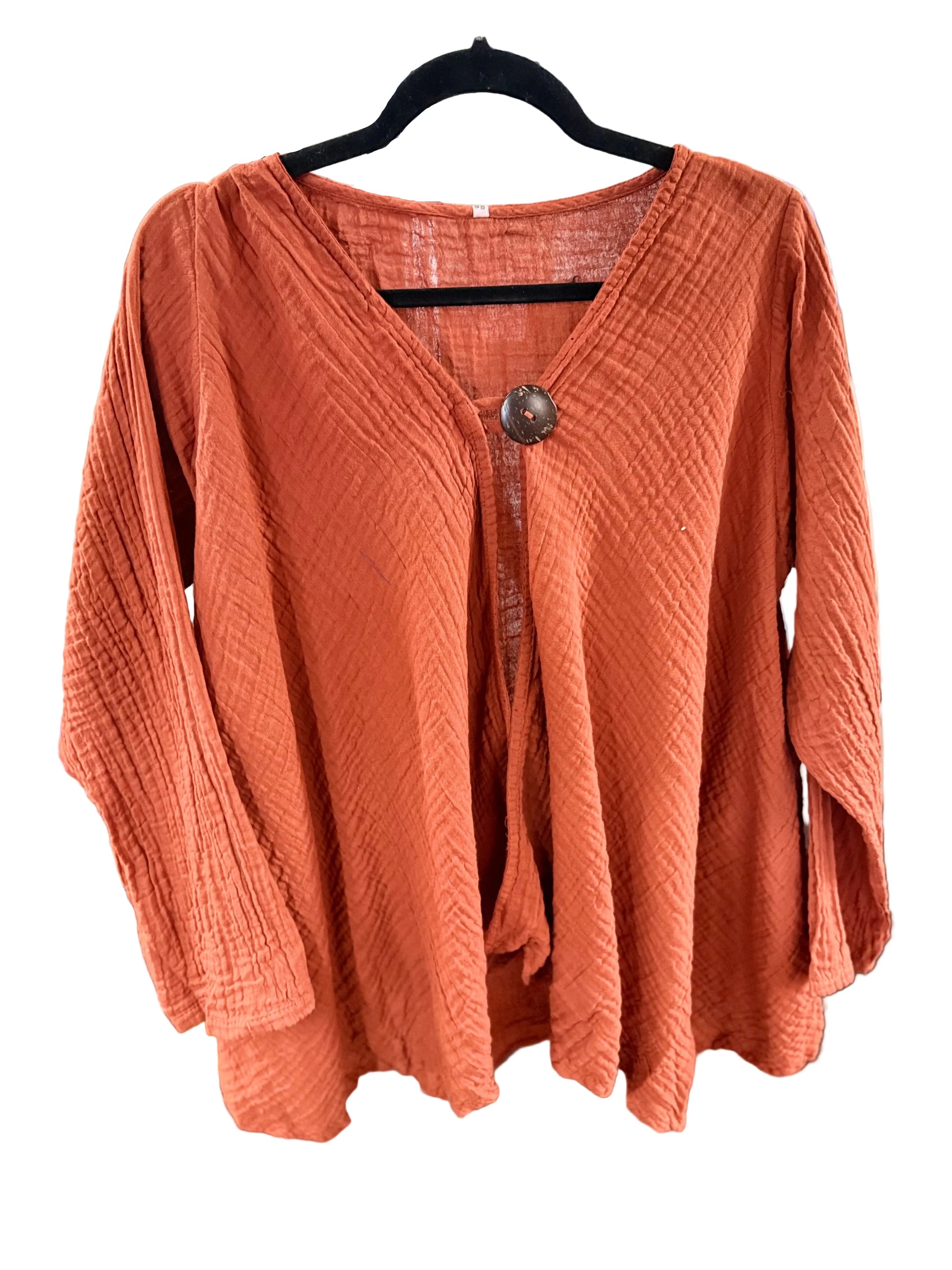 An reddish-orange textured crinkle gauze long-sleeve top with a V-neck and a single decorative button, hanging on a black hanger in a white background.