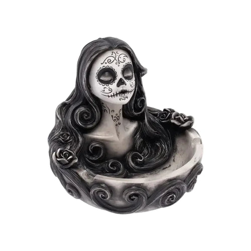 A gothic Day of the Dead skull figurine of a woman with long black hair rising from a bowl, set against a plain white background.